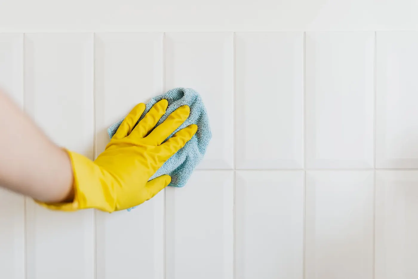 Yellow-gloved hand wiping clean white bathroom tiles